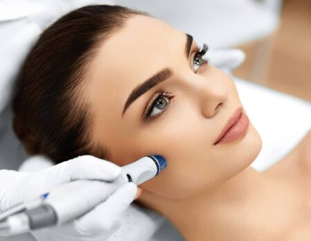 Une femme recevant un traitement facial avec un appareil, montrant un professionnel en soins de la peau. La scène met en avant des détails sur le visage et la technologie utilisée pour le soin. Hydrafacial Paris.